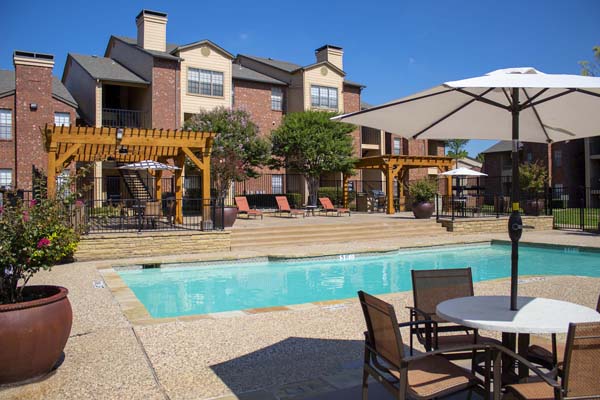 Apartment complex with a sparkling swimming pool w/ covered tables and seating.